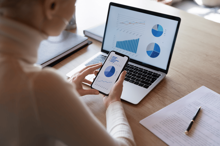 A woman looks at her phone and computer, looking at financial charts A woman looks at her phone and computer, looking at financial charts