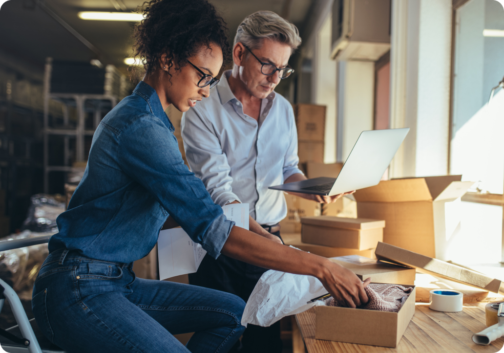 two people working together on a computer and packing items into a box