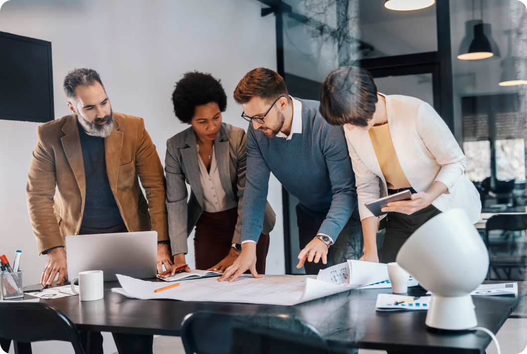 Four people leaning over a tables with papers on it working together